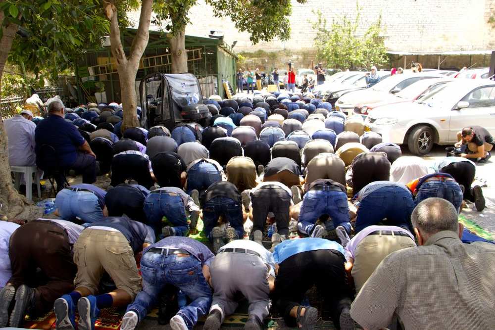 Musulmanes participan en las oraciones del mediodía en un estacionamiento cerca de la Puerta de los Leones en la Ciudad Vieja de Jerusalén, negándose a entrar en el recinto del Monte del Templo para llegar a la Mezquita de Al-Aqsa el 25 de julio de 2017. (Dov Lieber / Times of Israel)