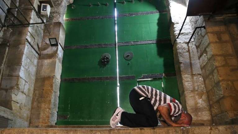 Un hombre musulmán reza frente a una puerta cerrada que conduce al Monte del Templo en la Ciudad Vieja de Jerusalén el 26 de julio de 2017. AFP / AHMAD GHARABLI)