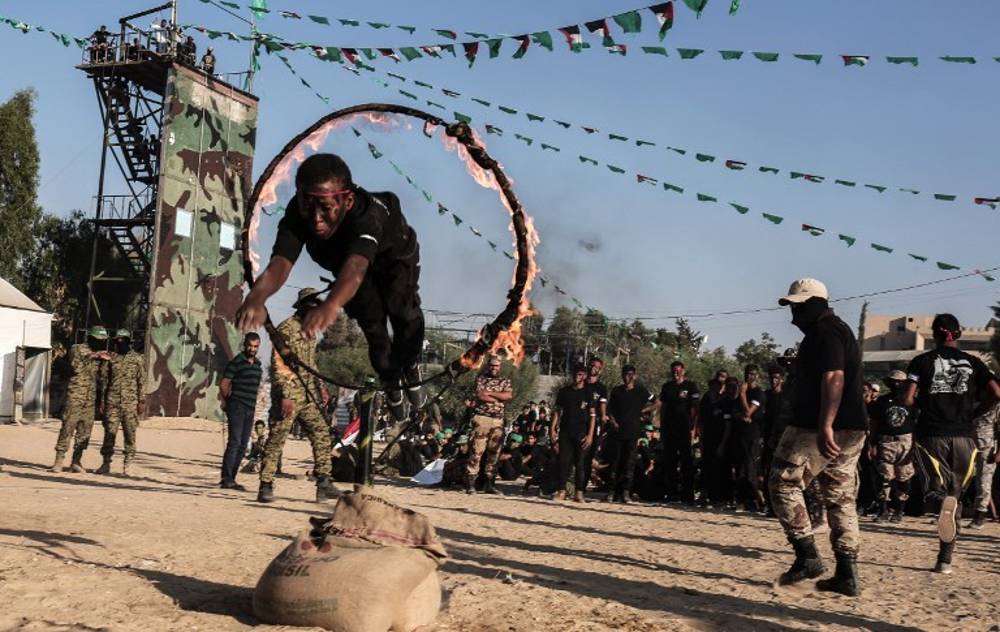 Jóvenes árabes saltan a través de un anillo de fuego durante una ceremonia militar de graduación en un campamento de verano de Hamás en Khan Yunis, en el sur de la Franja de Gaza, el 18 de agosto de 2017. (AFP PHOTO / SAID KHATIB)