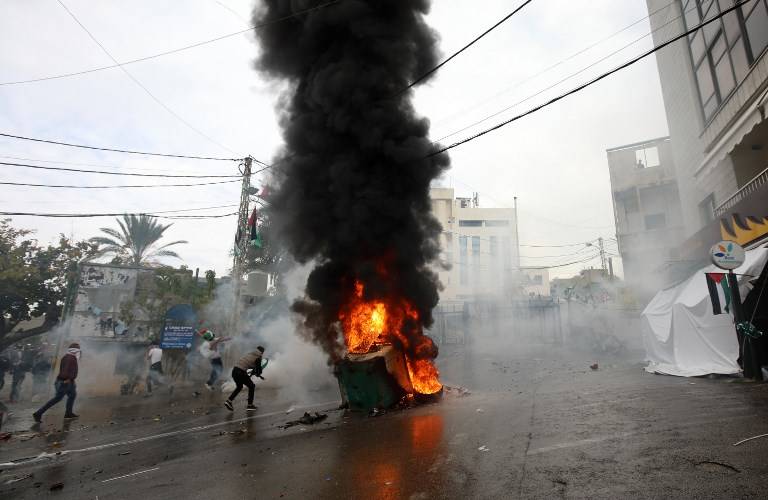 Fuerzas de seguridad libanesas disparan gases lacrimógenos para dispersar a los manifestantes mientras un incendio arde en un contenedor de basura durante una manifestación frente a la embajada de Estados Unidos en Awkar, en las afueras de la capital libanesa, Beirut, el 10 de diciembre de 2017. (AFP / ANWAR AMRO)