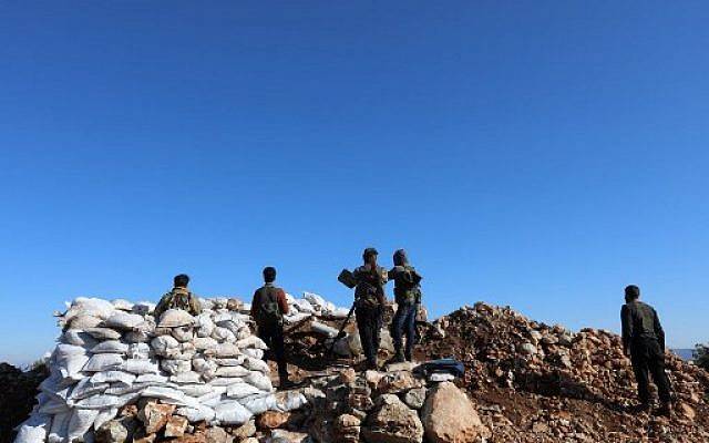 Una fotografía tomada el 20 de enero de 2018, desde la aldea de Qilah en la provincia de Idlib, muestra a combatientes rebeldes sirios de pie cerca del enclave kurdo de Afrin. (AFP PHOTO / OMAR HAJ KADOUR)