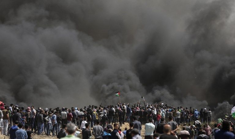 Hombres palestinos agitan sus banderas de la revuelta árabe en la versión de la AP, mientras el humo se eleva por la quema de neumáticos en la frontera entre Israel y Gaza durante una protesta, al este de la ciudad de Gaza en la Franja de Gaza, el 6 de abril de 2018. (AFP PHOTO / MAHMUD HAMS)