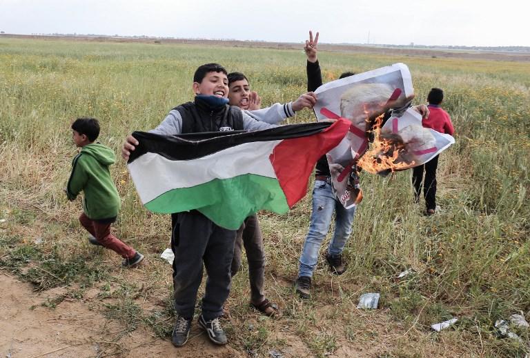 Niños palestinos manipulan fuego ante la mirada de sus padres mientras queman una foto del presidente estadounidense Donald Trump, como parte de la ola de incitación y uso de escudos humanos en la Franja de Gaza. (AFP PHOTO / SAID KHATIB)