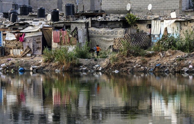 Una foto tomada el 1 de junio de 2018 muestra a una niña corriendo más allá de chozas cerca de una piscina de aguas negras en un barrio pobre de la ciudad de Gaza. (AFP / Mahmud Hams)