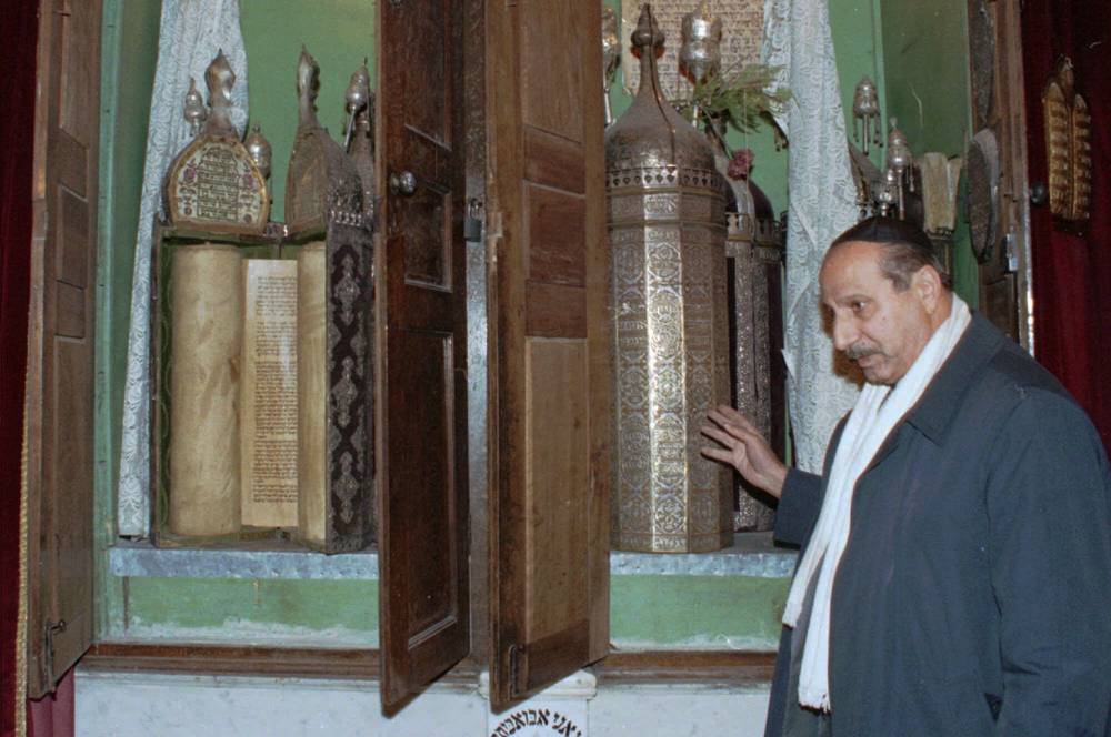 En esta foto de archivo del 21 de enero de 2000, Youssef Jajati, un líder de la comunidad judía en Siria, apunta a los rollos de la Torá conservados en un contenedor de plata en la sinagoga Jobar en Damasco. (AP Photo / Bassem Tellawi, Archivo)