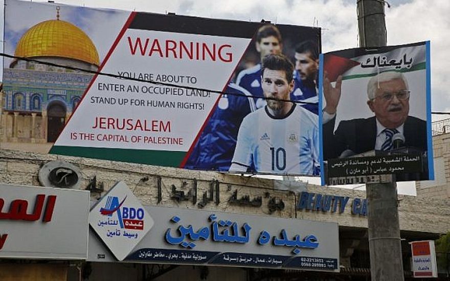 Este 5 de junio de 2018, la imagen muestra un cartel erigido en la ciudad cisjordana de Hebrón llamando a boicotear a la estrella de fútbol Lionel Messi (l) junto a un retrato del presidente de la Autoridad Palestina Mahmoud Abbas