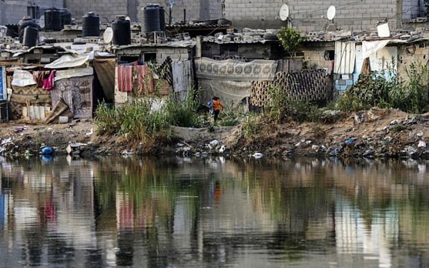 Una foto tomada el 1 de junio de 2018 muestra a una niña corriendo más allá de casuchas cerca de una piscina de aguas negras en un barrio pobre de la ciudad de Gaza. (AFP / Mahmud Hams)