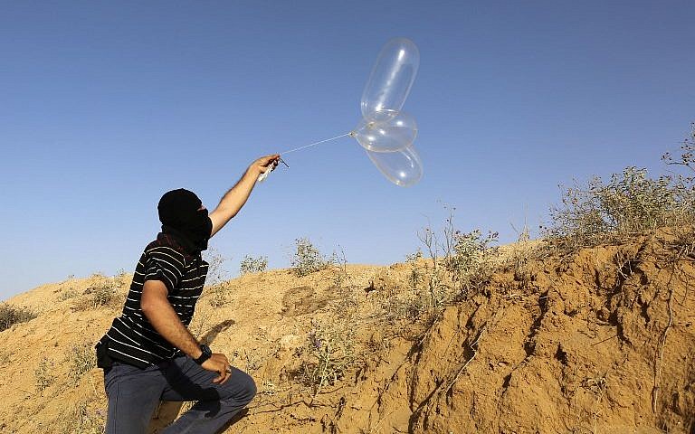 Ilustrativo: un palestino enmascarado lanza un globo cargado con materiales inflamables hacia Israel desde el pueblo de Rafah, al sur de Gaza, el 17 de junio de 2018. (AFP Photo / Said Khatib)