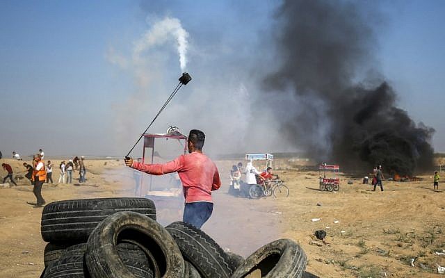 Un palestino utiliza un tirachinas para devolver un bote de gas lacrimógeno a las fuerzas israelíes durante los enfrentamientos a lo largo de la frontera al este de la ciudad de Gaza el 6 de julio de 2018. (AFP Photo / Said Khatib)