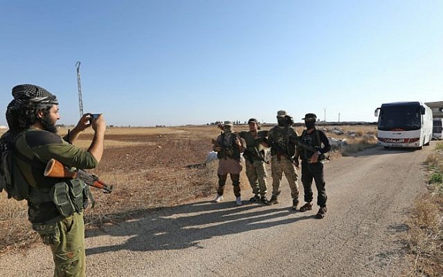 Los miembros del grupo Hayat Tahrir al-Sham, dirigido por el ex afiliado de Al-Qaeda en Siria, se toman una foto frente a un convoy de autobuses que se preparan para entrar a las ciudades de Fuaa y Kefraya para evacuar a sus residentes el 18 de julio de 2018. ( AFP PHOTO / OMAR HAJ KADOUR)