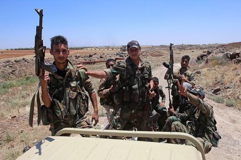 Los soldados de las fuerzas del gobierno sirio sostienen sus armas en la parte trasera de una camioneta durante una visita guiada por el gobierno en la aldea de al-Sourah, provincia de Daraa, el 29 de junio de 2018. (AFP PHOTO / Youssef KARWASHAN)