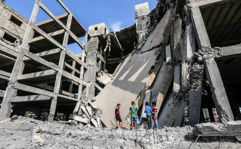 Niños palestinos caminan a través de los restos de un edificio de Hamás que fue dañado por los ataques aéreos israelíes en la ciudad de Gaza el 15 de julio de 2018. (AFP / MAHMUD HAMS)