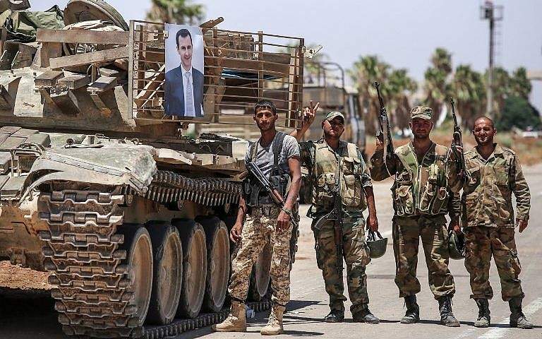 Soldados del régimen sirio se paran junto a la imagen del presidente sirio Bashar Assad colgando de un tanque en el cruce fronterizo de Nassib con Jordania en la provincia sureña de Daraa el 7 de julio de 2018. (AFP Photo / Youssef Karwashan)