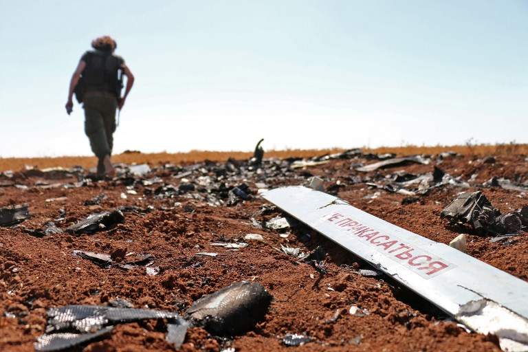 Un combatiente rebelde camina cerca de lo que supuestamente son los restos de un avión no tripulado del régimen sirio que fue derribado por Israel el día anterior, en un campo cerca de Barqah, a unas docenas de kilómetros de la frontera israelí el 12 de julio de 2018. (AFP PHOTO / Ahmad al-Msalam)