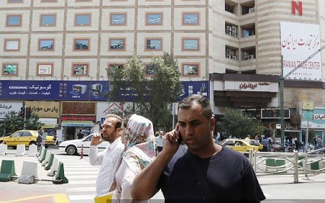 Un hombre habla por su teléfono móvil cuando cruza una calle en un distrito comercial en el centro de Teherán el 6 de agosto de 2018. (AFP PHOTO / ATTA KENARE)