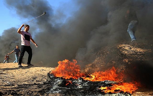 Un palestino usa un tirachinas junto a la quema de neumáticos durante los enfrentamientos en la frontera entre Israel y Gaza, al este de Khan Yunis en el sur de la Franja de Gaza el 10 de agosto de 2018. (AFP Photo / Said Khatib)