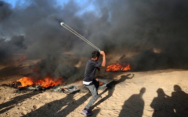 Un manifestante palestino usa un tirachinas junto a neumáticos en llamas durante una manifestación en la frontera entre Israel y Gaza, al este de Khan Yunis en el sur de la Franja de Gaza el 10 de agosto de 2018. (AFP PHOTO / SAID KHATIB)