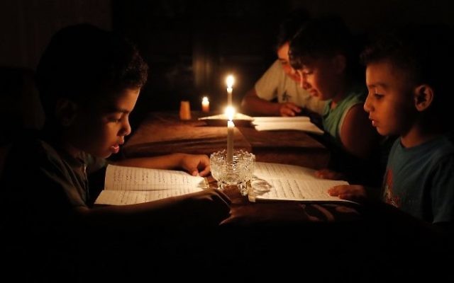 Una imagen tomada el 13 de junio de 2017 muestra a los niños palestinos en casa leyendo libros a la luz de las velas debido a la escasez de electricidad en la ciudad de Gaza. (AFP / THOMAS COEX)