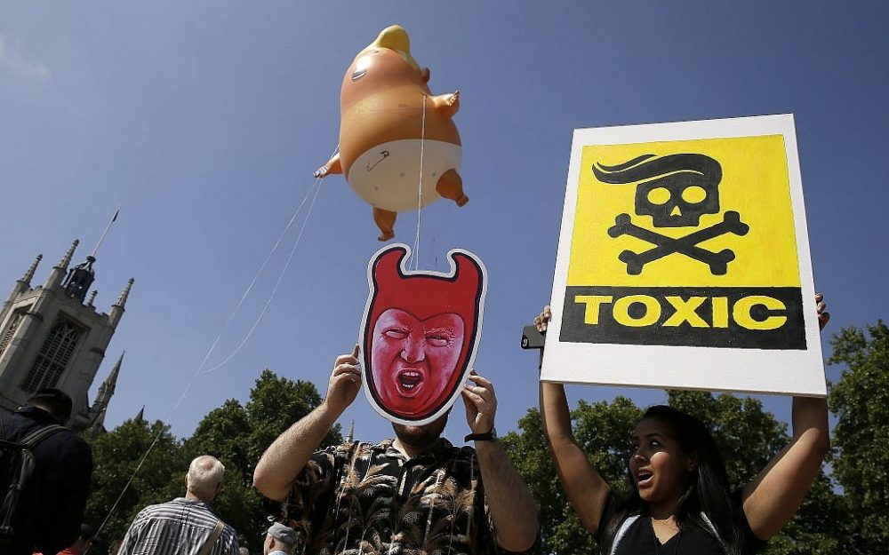 Los manifestantes levantan pancartas mientras un dirigible no tripulado de dibujos animados de seis metros del presidente estadounidense Donald Trump vuela como protesta contra su visita, en Parliament Square en Londres, Inglaterra, el viernes 13 de julio de 2018. (AP Photo / Tim Ireland)