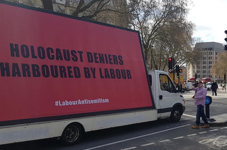 Keith Walker involucra al conductor de una furgoneta que transporta una cartelera sobre el antisemitismo en el Partido Laborista en la Plaza del Parlamento de Londres, el 17 de abril de 2018. (Cnaan Liphshiz / JTA)