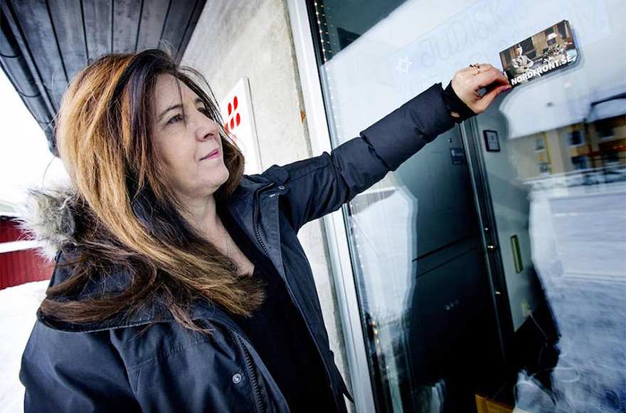 Carinne Sjoberg pelando una pegatina que los neonazis dejaron en la puerta de lo que solía ser el centro comunitario judío de Umea, Suecia. (Cortesía de Sjoberg / vía JTA)