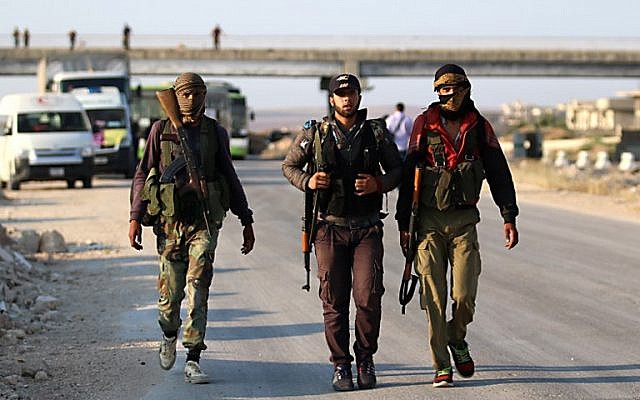 Los combatientes rebeldes sirios de la provincia de Quneitra caminan con sus rifles mientras esperan en el punto de cruce de Morek para ser transferidos en las provincias de Idlib y Aleppo el 21 de julio de 2018. (AFP Photo / Aaref Watad)