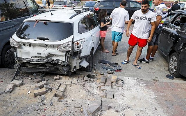 La gente se para junto a un automóvil que resultó dañado después de que un cohete disparado por terroristas de la Franja de Gaza cayó en la ciudad de Sderot, al sur de Israel, el 9 de agosto de 2018. (JACK GUEZ / AFP)