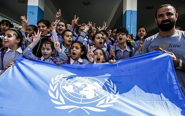 Los escolares palestinos gritan consignas y levantan el gesto de victoria sobre una bandera de la ONU durante una protesta en una escuela de la Agencia de Socorro y Obras de las Naciones Unidas (UNRWA), financiada por US AID, en el campamento de refugiados de Arroub cerca de Hebrón en Cisjordania el 5 de septiembre. 2018. (AFP / Hazem Bader)