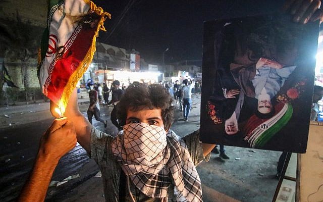 Un manifestante iraquí sostiene una bandera iraní mientras otra le prendió fuego, junto a un retrato que representa a los antiguos y actuales líderes supremos, los ayatolá Jomeini y Jamenei, durante las manifestaciones contra el gobierno y la falta de servicios básicos en Basora el 7 de septiembre de 2018. (AFP Photo / Haidar Mohammad Ali)