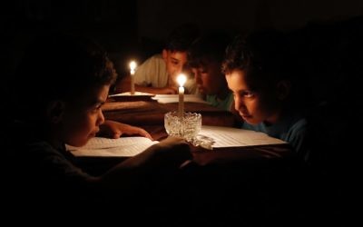 Niños palestinos en casa leyendo libros a la luz de las velas debido a la escasez de electricidad en la ciudad de Gaza, 13 de junio de 2017. (AFP / Thomas Coex)