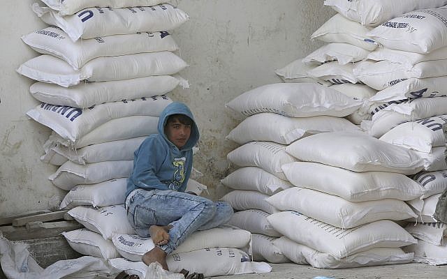 Un palestino se sienta en sacos de harina mientras espera recibir ayuda alimentaria del centro de distribución de alimentos de la ONU en el campo de refugiados de Nusseirat, en el centro de la Franja de Gaza, el 17 de enero de 2018. (AP Photo / Adel Hana)