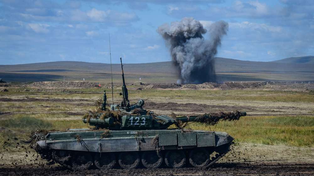 Un T-90 en el primer plano; una explosión por detrás
