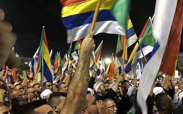 Manifestantes agitan banderas israelíes y drusas en una manifestación contra la ley del estado-nación, en la plaza Rabin de Tel Aviv el 4 de agosto de 2018. (Personal de Luke Tress / Times of Israel)