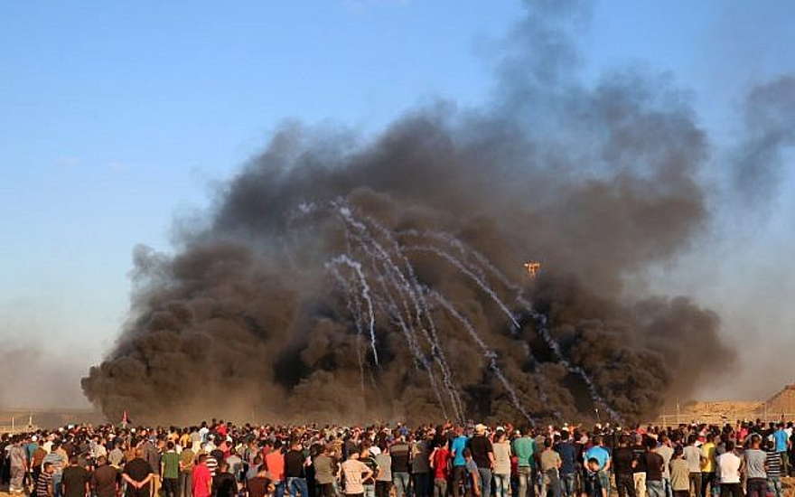 El 12 de octubre de 2018, terroristas palestinos se reúnen en el humo que se alza al quemar llantas cuando las fuerzas israelíes lanzan botes de gas lacrimógeno a la frontera entre Israel y Gaza, al este de la ciudad de Gaza. (Foto de SAID KHATIB / AFP)