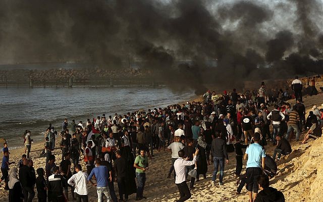 Los palestinos se reúnen en la playa mientras otros queman neumáticos cerca de la cerca de la frontera de la Franja de Gaza con Israel cerca de Beit Lahiya, , 29 de octubre de 2018. (Adel Hana / AP)