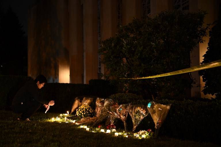 Un hombre se arrodilla para encender una vela debajo de un cordón policial fuera de la Sinagoga Árbol de la Vida en Pittsburgh, después de un tiroteo que dejó 11 muertos el 27 de octubre de 2018 (Brendan Smialowski / AFP)