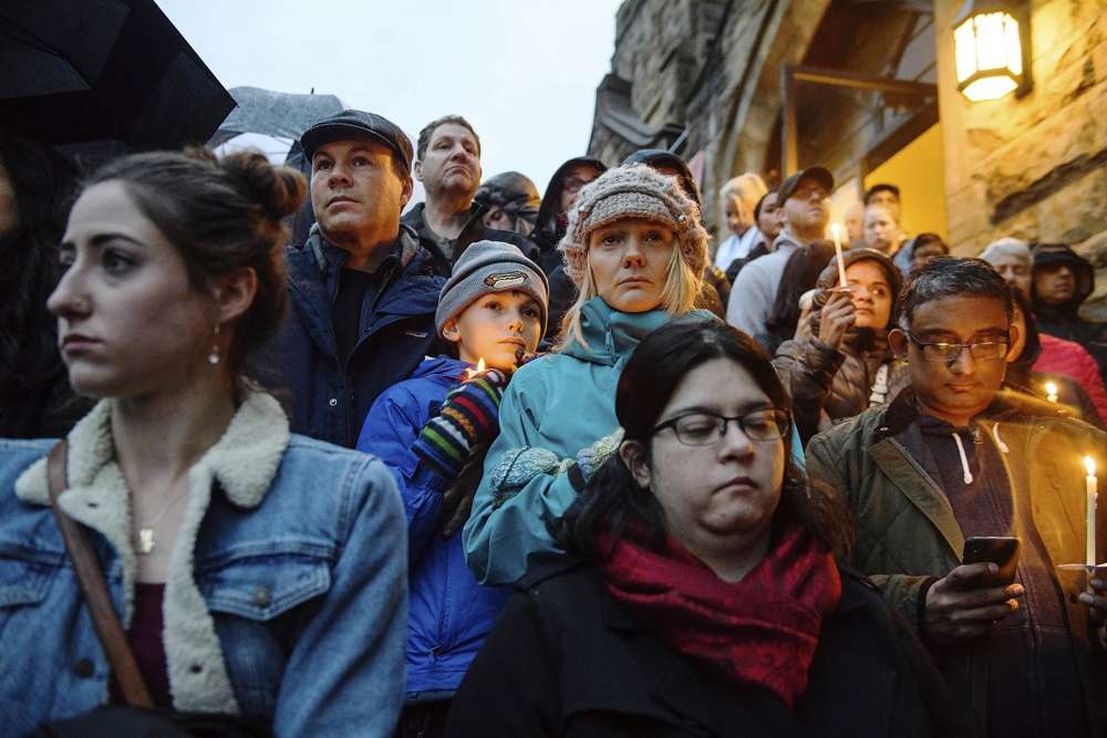 La gente se para en las escaleras de la Sexta Iglesia Presbiteriana mientras la multitud se desplaza cuesta arriba por la colina y por la calle para ver unas cuadras desde donde un hombre armado disparó y mató a 11 fieles en la sinagoga de la Congregación Árbol de la Vida el sábado 27 de octubre de 2018, en el Squirrel Hill sección de Pittsburgh, Pennsylvania. (Stephanie Strasburg / Pittsburgh Post-Gazette a través de AP)