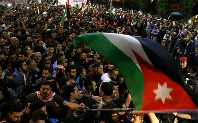 Los manifestantes ondean una bandera jordana frente a los oficiales de policía jordanos durante una protesta cerca de la oficina del primer ministro en Amman, Jordania, el 5 de junio de 2018. (AFP PHOTO / Khalil MAZRAAWI)