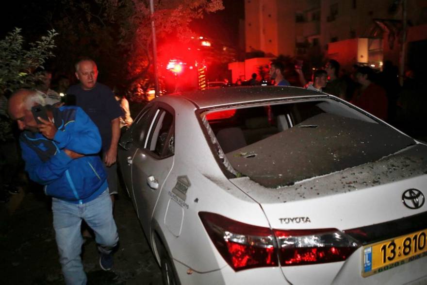 Dos hombres pasan por delante de un vehículo que fue alcanzado por un cohete disparado desde la Franja de Gaza, en la ciudad de Ashkelon, al sur de Israel, el 12 de noviembre de 2018. (GIL COHEN-MAGEN / AFP)