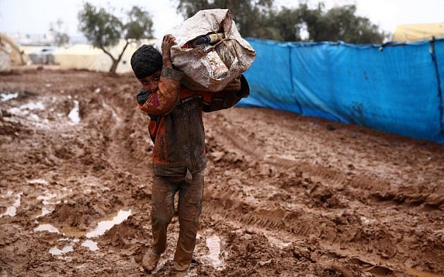 Un niño sirio carga un saco en su hombro mientras camina en el lodo en un campamento de desplazamientos en las afueras de Shamarin, cerca de la frontera con Turquía en la provincia norteña de Aleppo, el 6 de diciembre de 2018. (Nazeer AL-KHATIB / AFP)