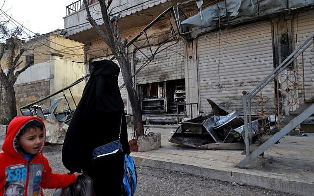 Una mujer y un niño sirios pasan frente a las puertas cerradas de un restaurante donde se produjo un ataque suicida contra las fuerzas de la coalición liderada por Estados Unidos en la ciudad de Manbij, en el norte de Siria, que mató a cuatro militares estadounidenses el día anterior el 17 de enero de 2019. Delil SOULEIMAN / AFP)