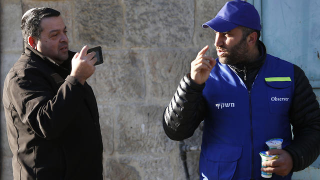 El colono israelí, a la izquierda, toma una foto de un observador palestino mientras vigila a los niños que caminan a la escuela en la ciudad cisjordana de Hebrón.