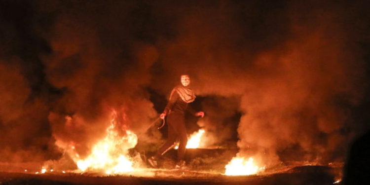 Un terrorista enmascarado tira un neumático en llamas durante un ataque nocturno cerca de la valla a lo largo de la frontera con Israel, al este de la ciudad de Gaza, el 11 de febrero de 2019. (Mahmud Hams / AFP)