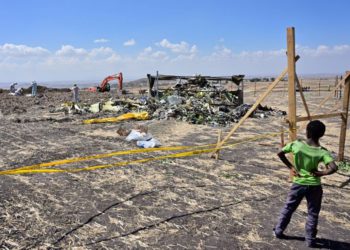 Un niño parece que los investigadores forenses peinan el suelo en busca de pruebas de ADN cerca de una pila de escombros retorcidos del avión en el lugar del accidente de un avión Boeing 737 MAX operado por las vías aéreas etíopes el 16 de marzo de 2019 en la aldea de Hama Quntushele cerca de Bishoftu en la región de Oromia. (TONY KARUMBA / AFP)
