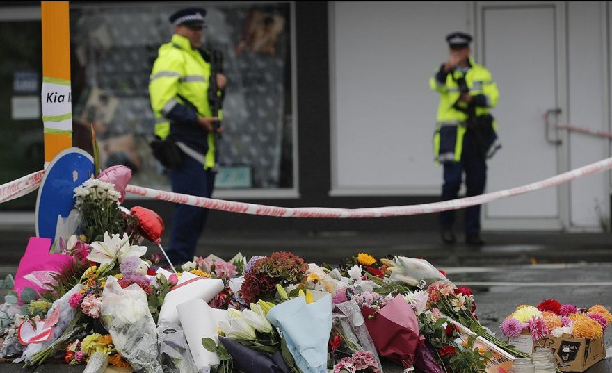 Flor descansa en un bloque de carretera, mientras dos agentes de policía montan guardia cerca del monumento improvisado cerca de la mezquita Linwood en Christchurch, Nueva Zelanda, sábado 16 de marzo de 2019. (AP / Vincent Thian)