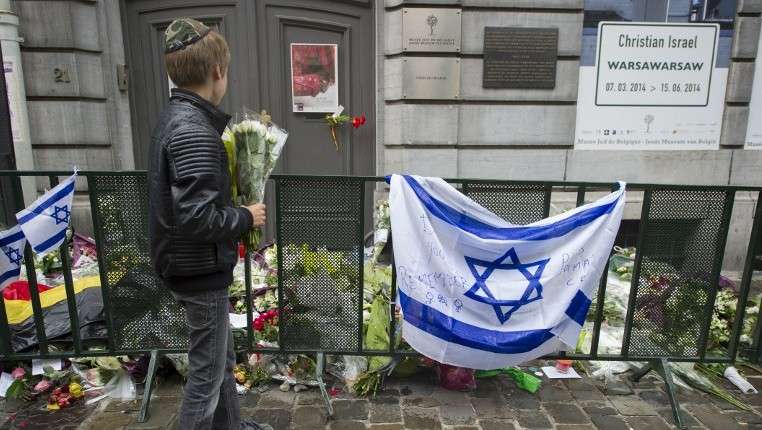 Un niño judío de pie con flores frente a una bandera israelí y flores colocadas fuera del Museo Judío en Bruselas, donde se produjo un tiroteo mortal dos días antes, 26 de mayo de 2014. (AFP / Belga / Anthony Dehez)