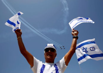 Un hombre ondea banderas de Israel mientras aviones de la Fuerza Aérea israelí vuelan en formación sobre el mar Mediterráneo durante un espectáculo aéreo como parte de las celebraciones por el Día de la Independencia de Israel con motivo del 70 aniversario de la creación del estado, en Tel Aviv, Israel, el 19 de abril. 2018 .. (crédito de foto: REUTERS / AMIR COHEN)