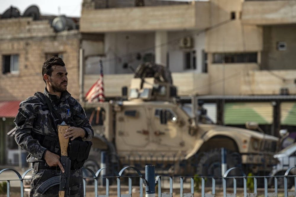 Un combatiente de las Fuerzas Democráticas Sirias SDF hace guardia mientras un vehículo militar estadounidense que sale de una base de las fuerzas estadounidenses en la ciudad siria del norte de Tal Tamr pasa el 20 de octubre de 2019 (Delil SOULEIMAN / AFP)