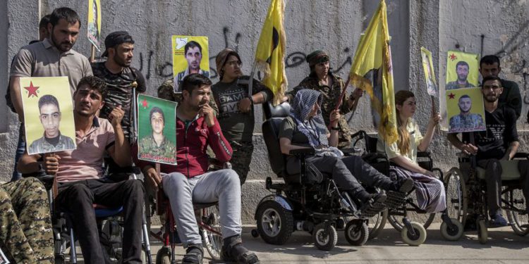 Los combatientes kurdos heridos tienen retratos de camaradas que fueron asesinados mientras luchaban contra el Estado Islámico, durante una manifestación contra una incursión turca prevista contra combatientes kurdos sirios, frente al edificio de las Naciones Unidas, en Qamishli, noreste de Siria, el lunes 8 de octubre de 2019. (Foto AP / Ahmad Baderkhan)