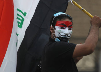Un manifestante iraquí con una máscara de Guy Fawkes con los colores de la bandera nacional ondea una bandera iraquí durante una manifestación antigubernamental en la capital, Bagdad, el 27 de octubre de 2019. (AFP)